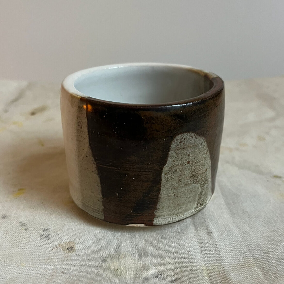 Handmade Ebony and Ivory cappuccino cup with a sharp vertical split between dark iron glaze and pale stone glaze