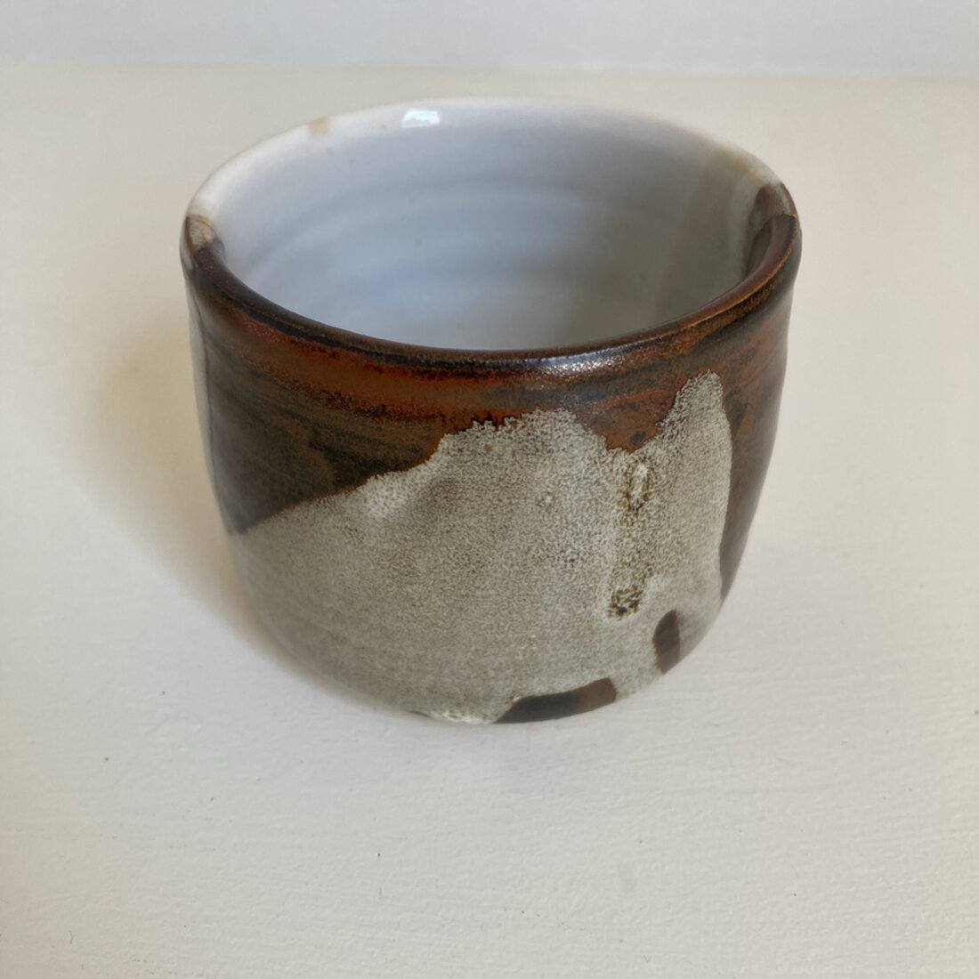 Medium handmade cup with iron brown glaze breaking to oatmeal speckle, white interior