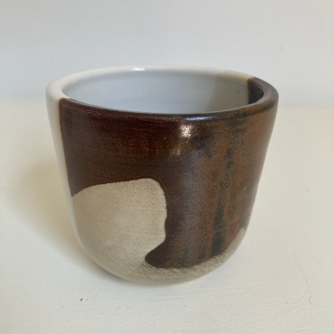 Medium handmade cup with iron brown glaze and a cream patch, white interior