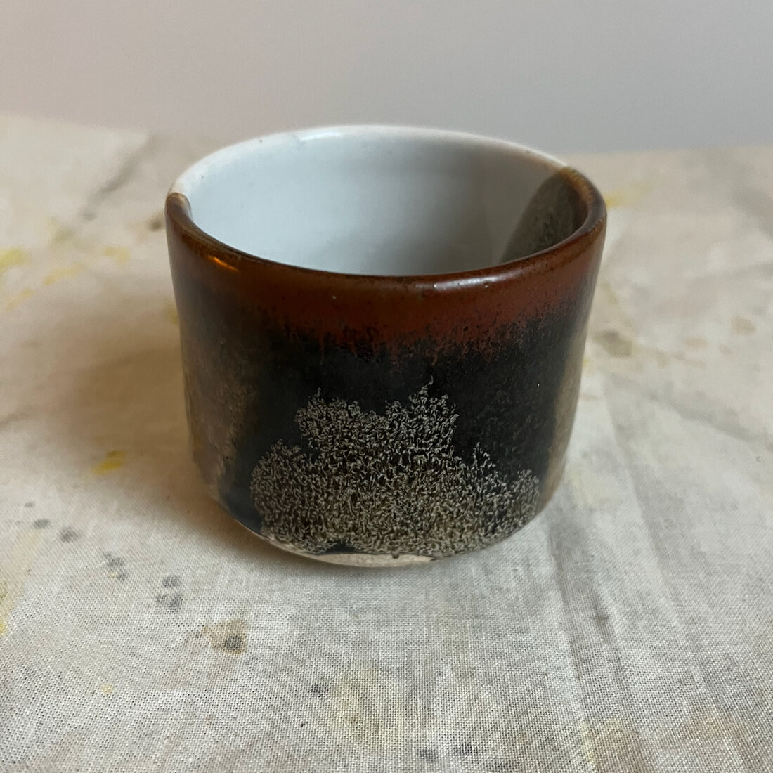 Handmade Paint Horse cappuccino cup with an irregular pale speckled patch breaking through a dark iron glaze