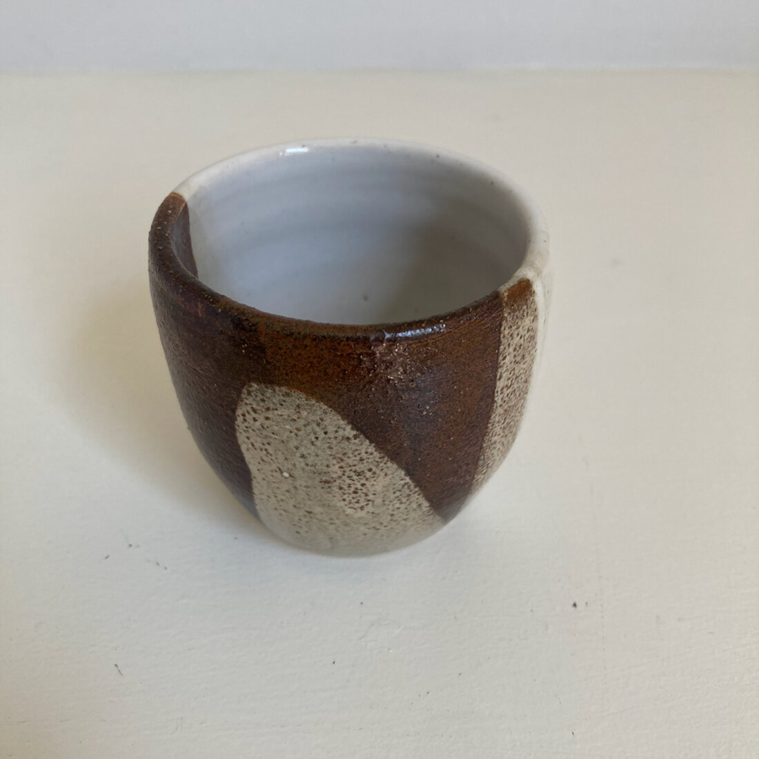 Small handmade cup with iron brown glaze breaking to cream, white interior