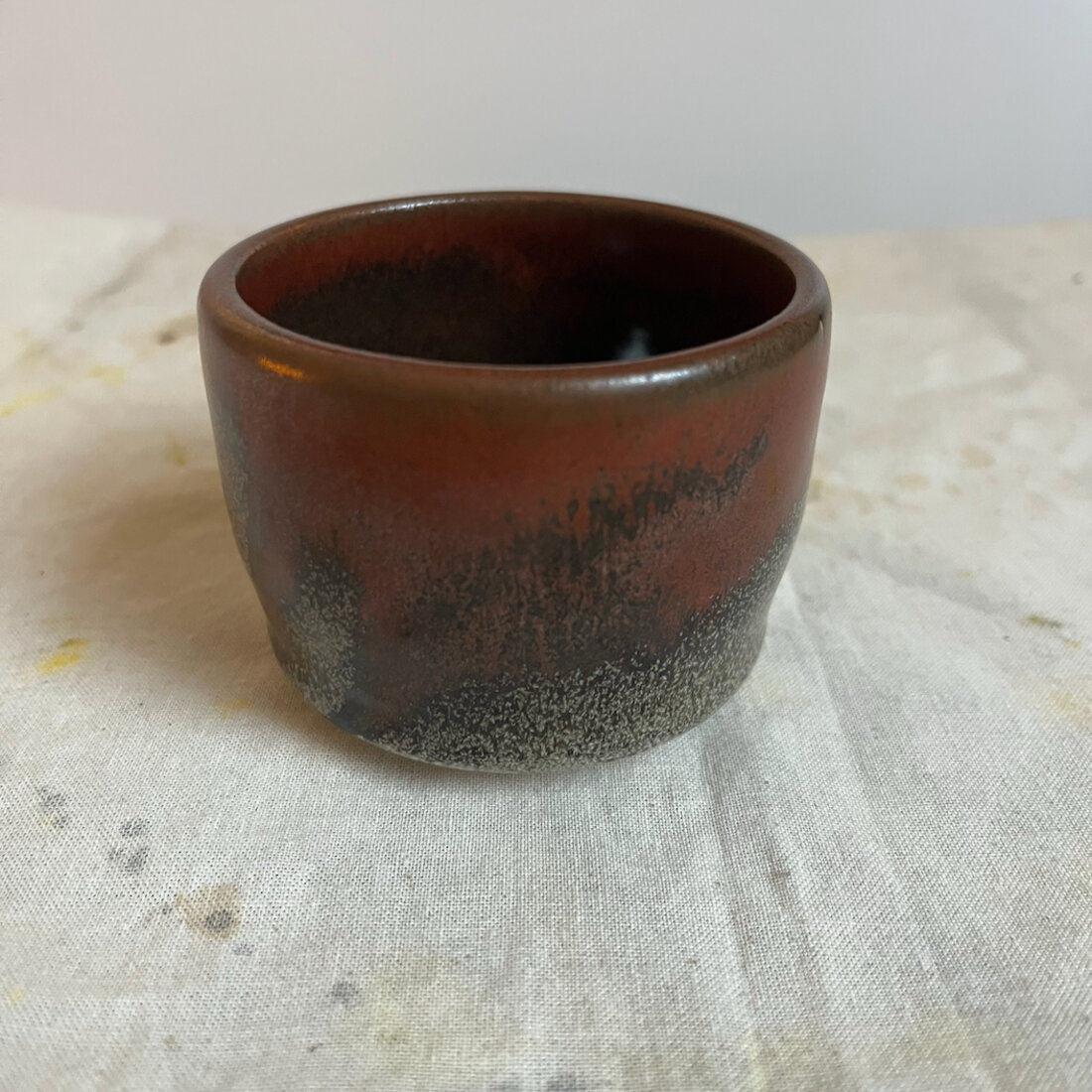Handmade Tenmoku cappuccino cup with deep red-brown glaze breaking to ash speckle at the base